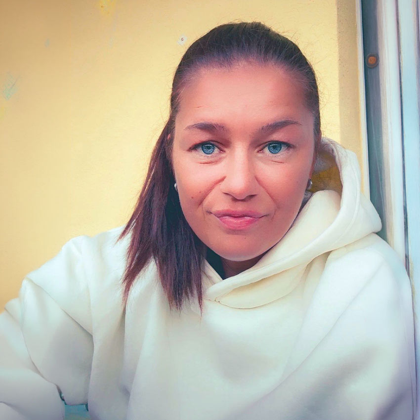 Eine Frau mit braunen Haaren trägt einen weißen Hoodie und wirkt entspannt