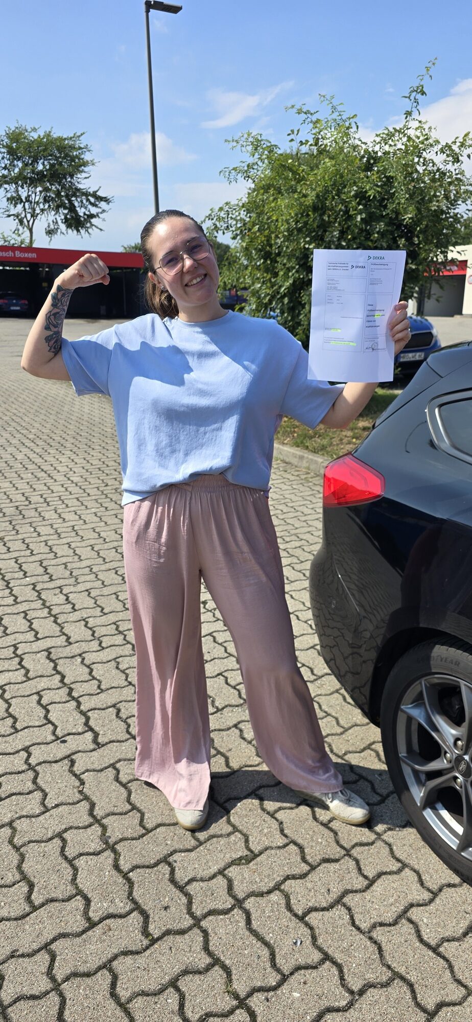 Stolze Frau mit Brille zeigt laechelnd DEKRA Dokument neben schwarzem Auto
